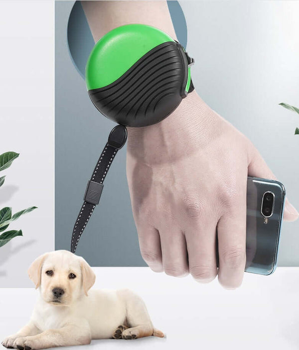 Wrist-type pet watch leash on a hand with smartphone, featuring a green and black design, next to a cute puppy.